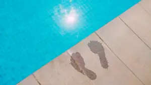Pool waterline tile and wet footprints on a sunny pool deck